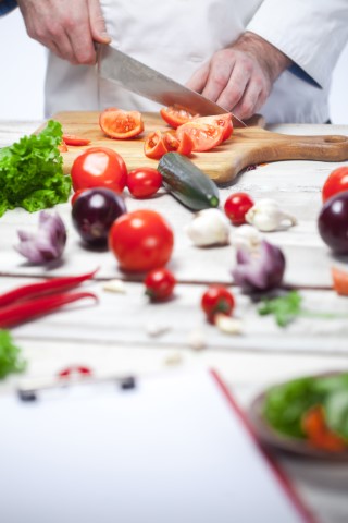 vegetables on a table with a hands in background cutting a pepper