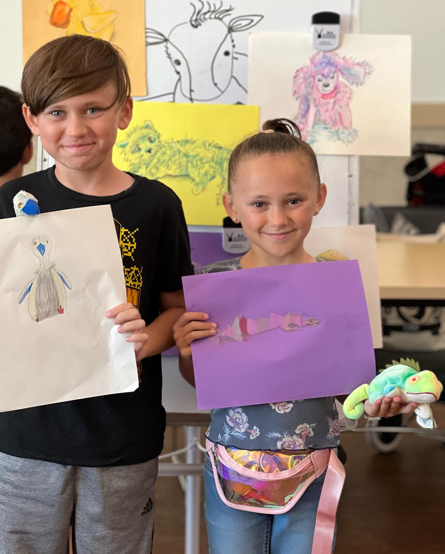 Two children holding a Beanie Baby and their artwork