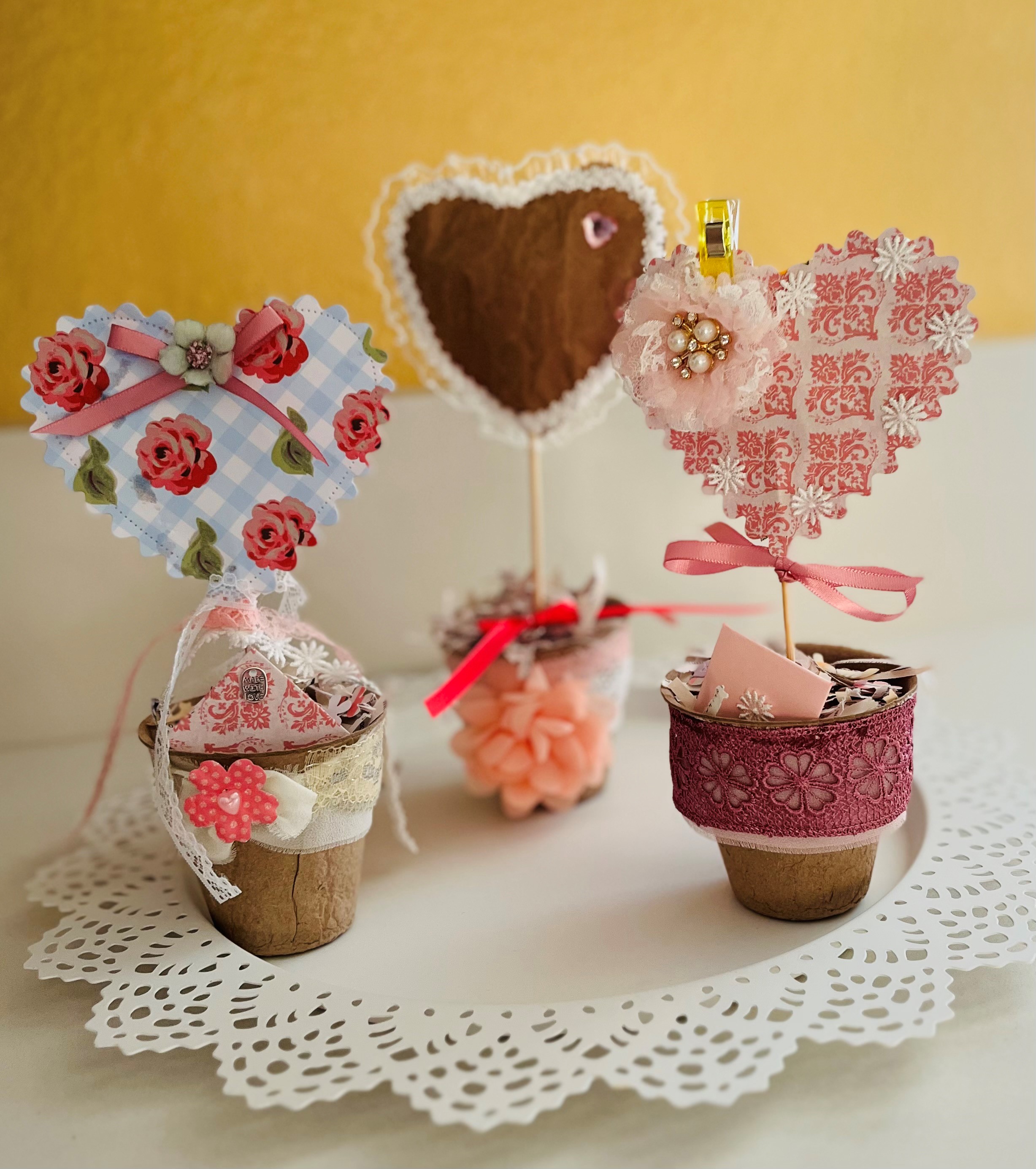 Valentine topiary samples, including a plant pot, lace paper pieces, and ribbon on a red background