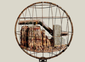 Image of a rusty pipe and rocks in a circular metal cage by artist Oscar Romo. 