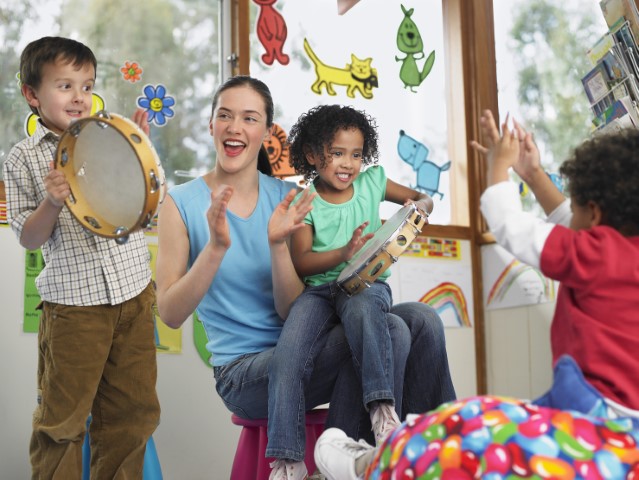 Woman with children clapping and playing with tambourines.
