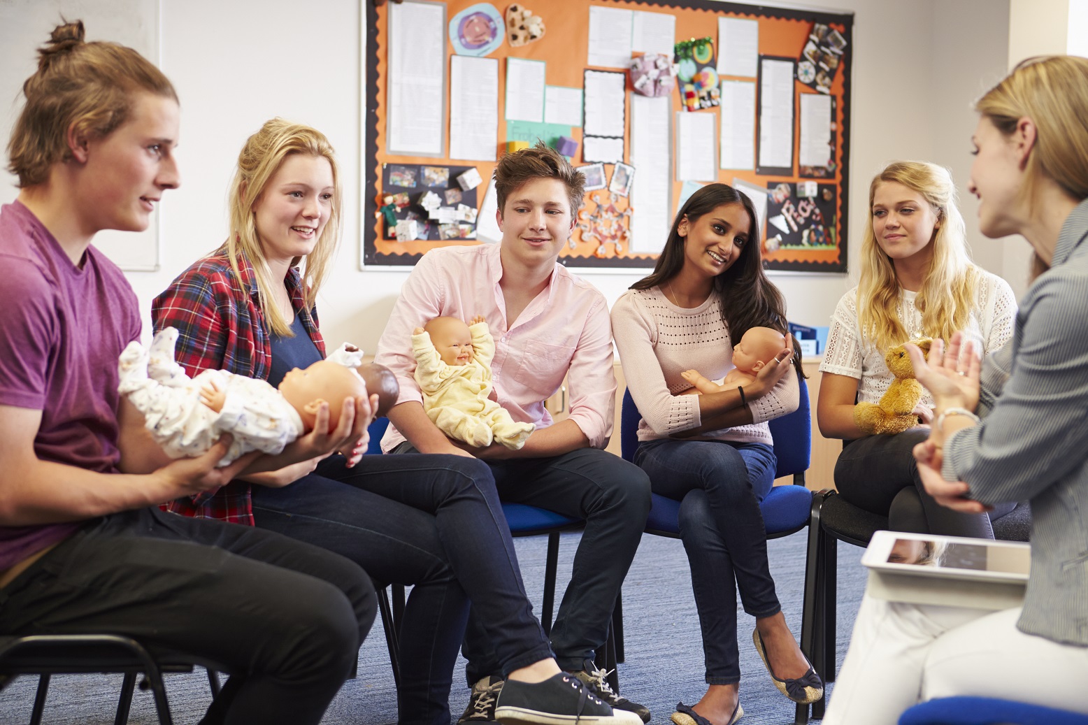 Young adults holding baby dolls in their laps during a childcare class