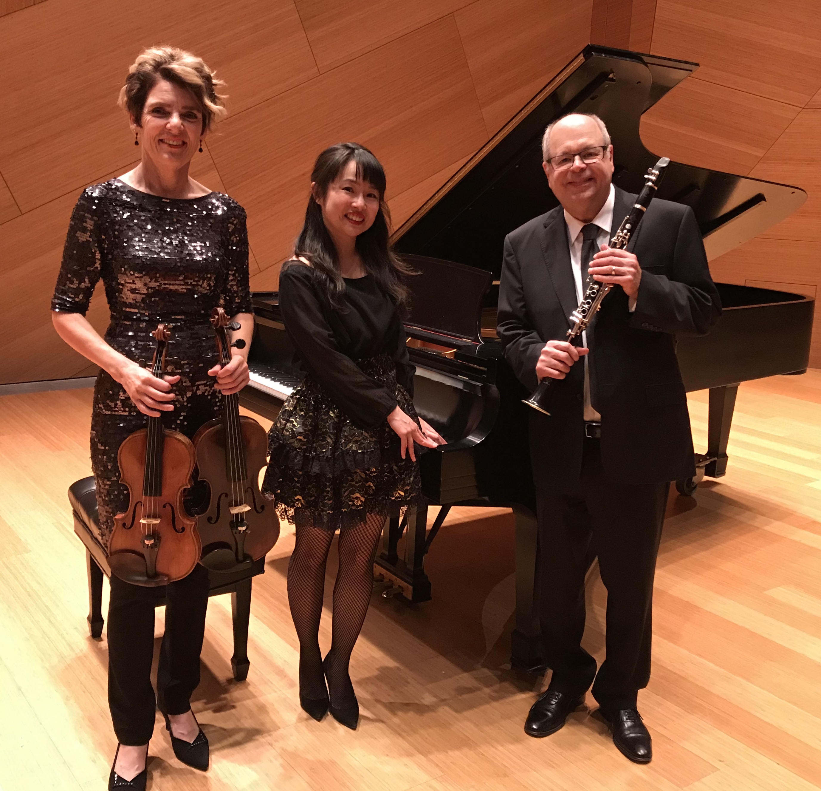 Three musicians standing in front of a grand piano