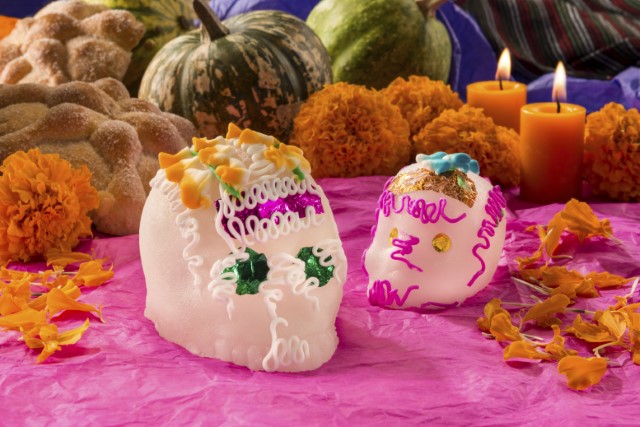Two sugar skulls on a pink tablecloth with pumpkins in the background