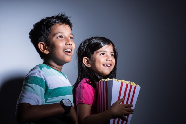 a boy and girl with faces lighted by a movie, girl holding a box of popcorn