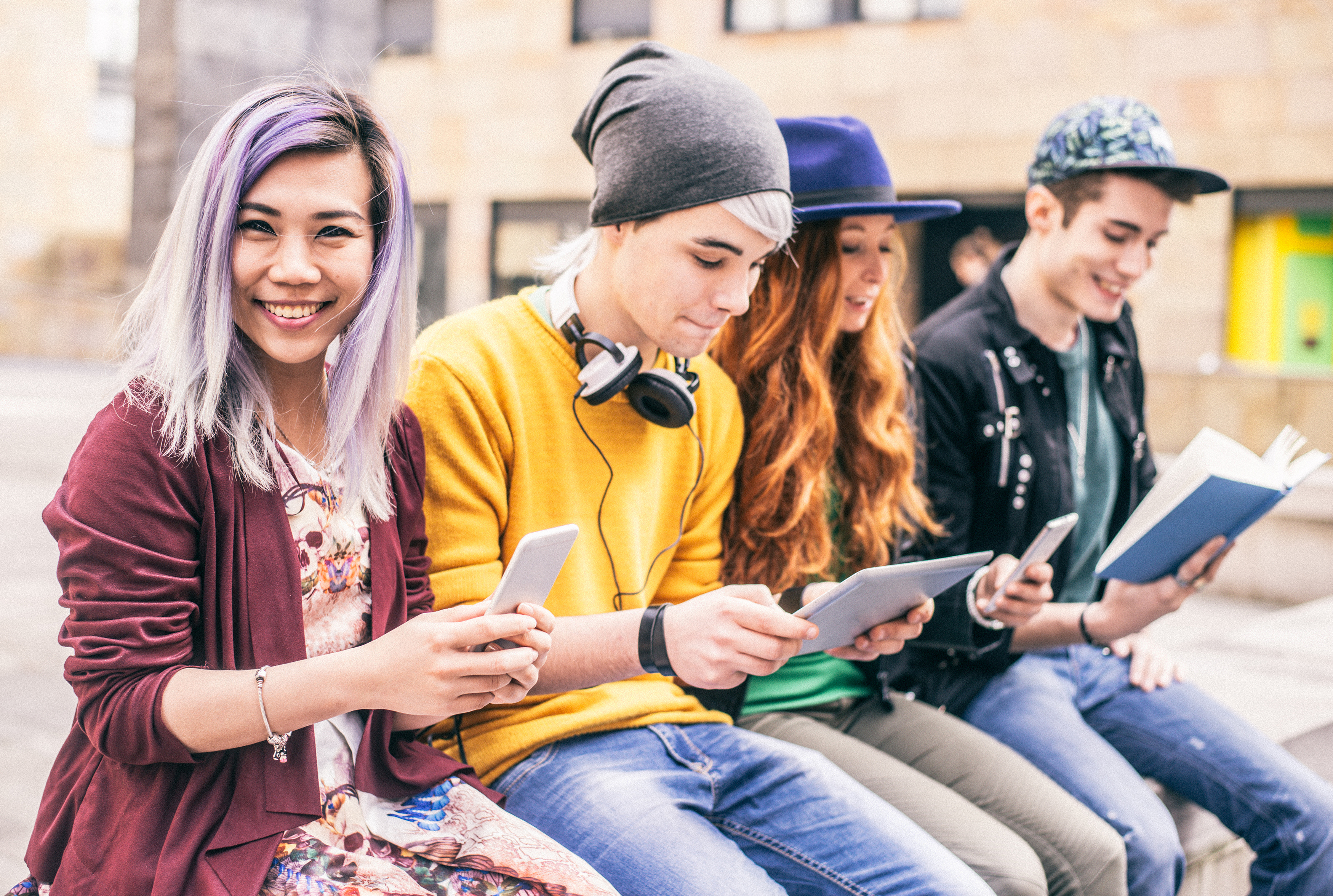 Four teens sitting on a wall, looking at books/mobile devices