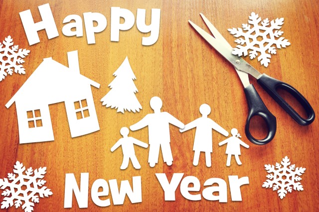 A pair of scissors and paper cutouts of a house, trees, people, snowflakes, and the words "Happy New Year"