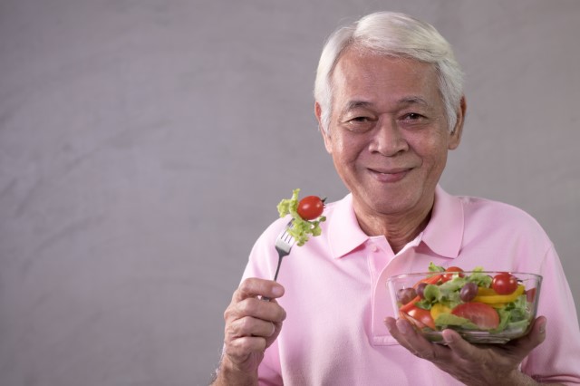 Elderly man eats a salad.