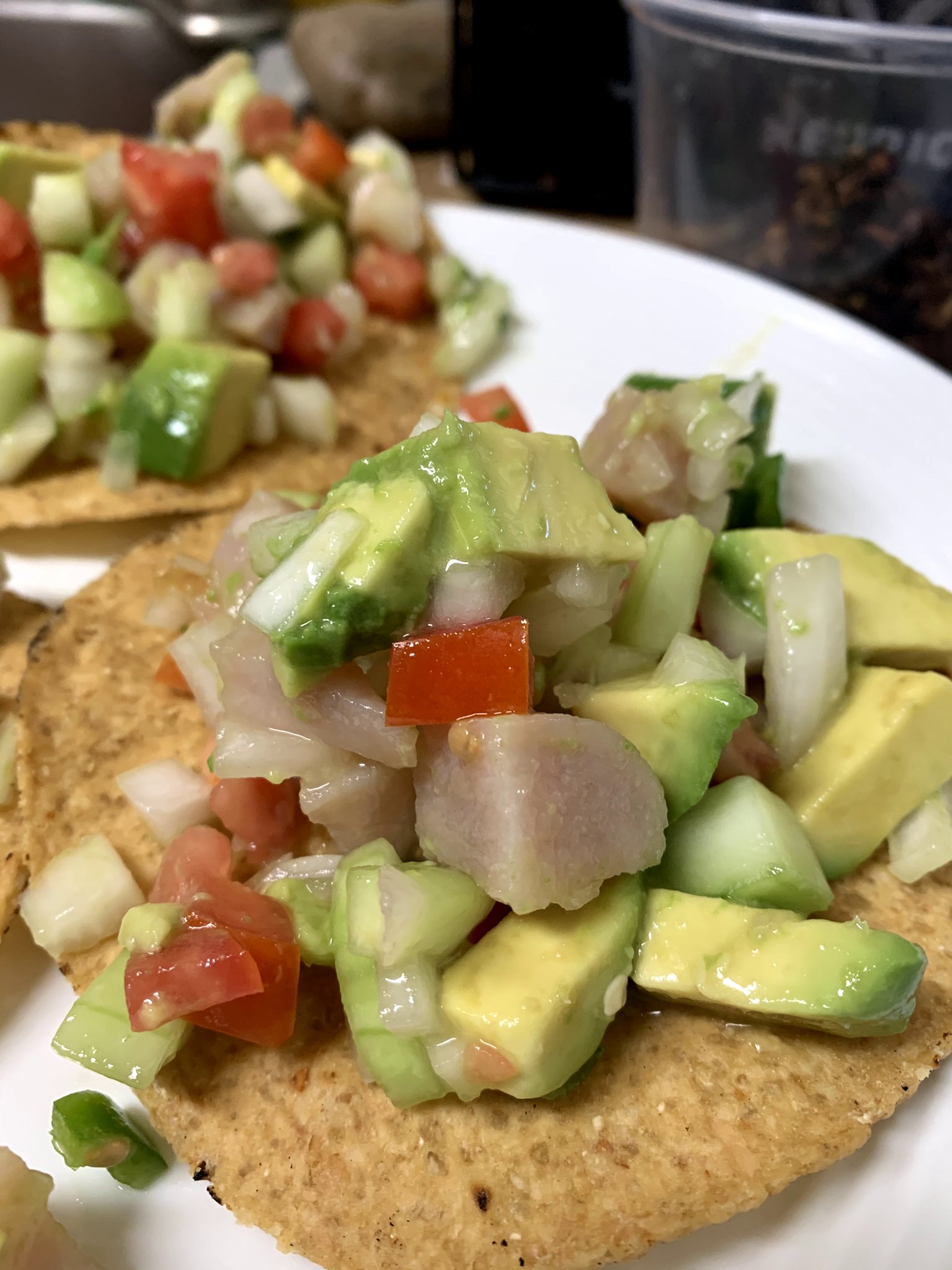 Diced fish, avocado, onion and tomato on top of a corn tostada