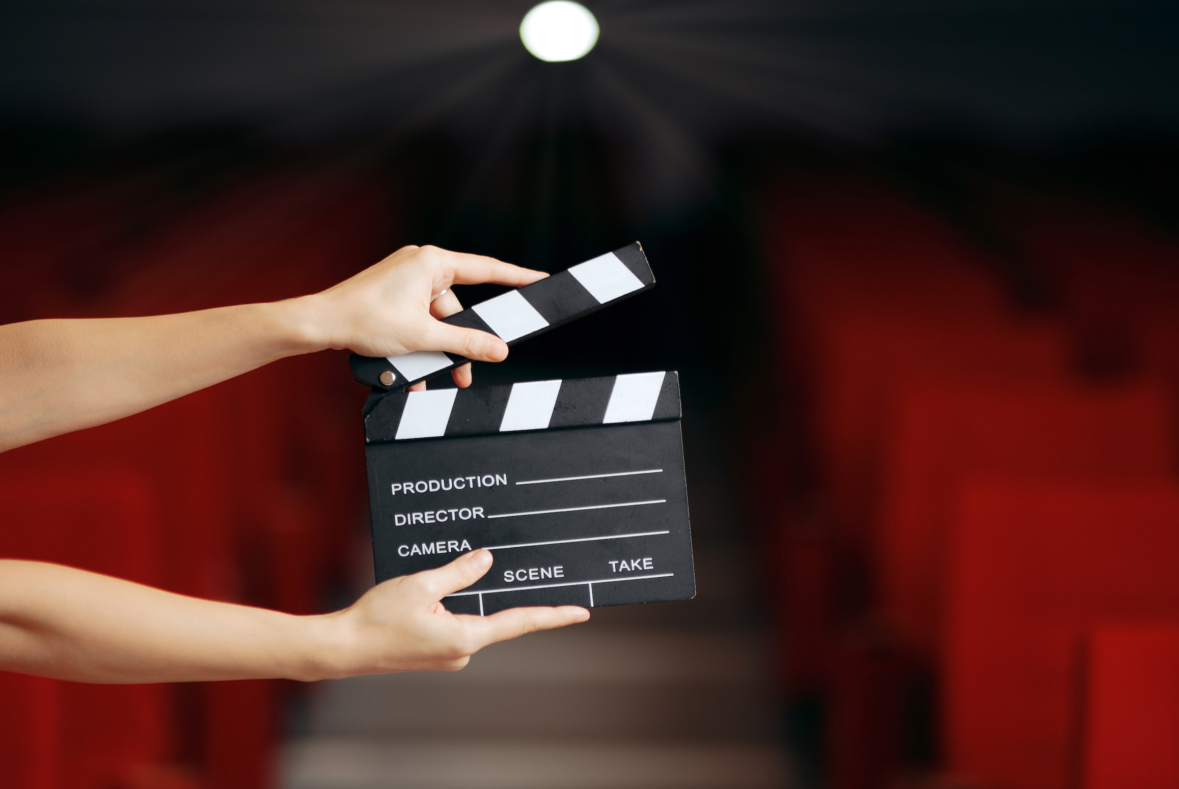 Hands holding a clapperboard in front of an empty theater