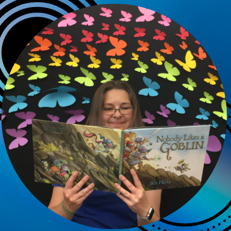 Ms. Carrie reading a picture book in front of a rainbow of butterflies. 