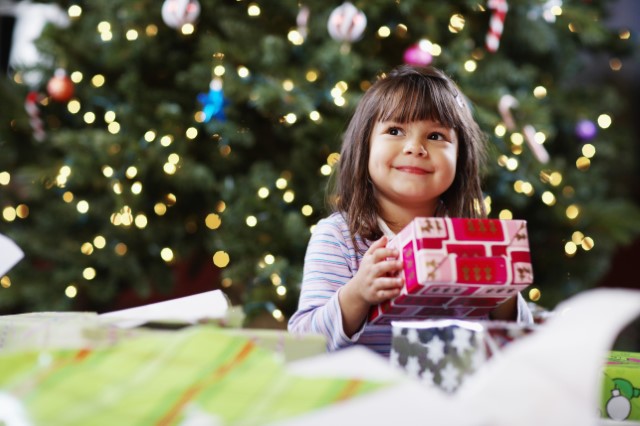 Little girl sitting in front of Christmas tree holding a gift