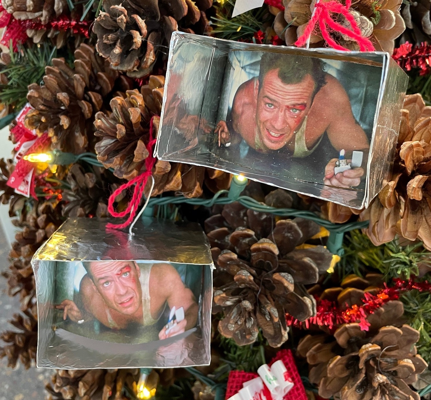 Tree with two ornaments that have photos of Bruce Willis crawling through a metal duct.  