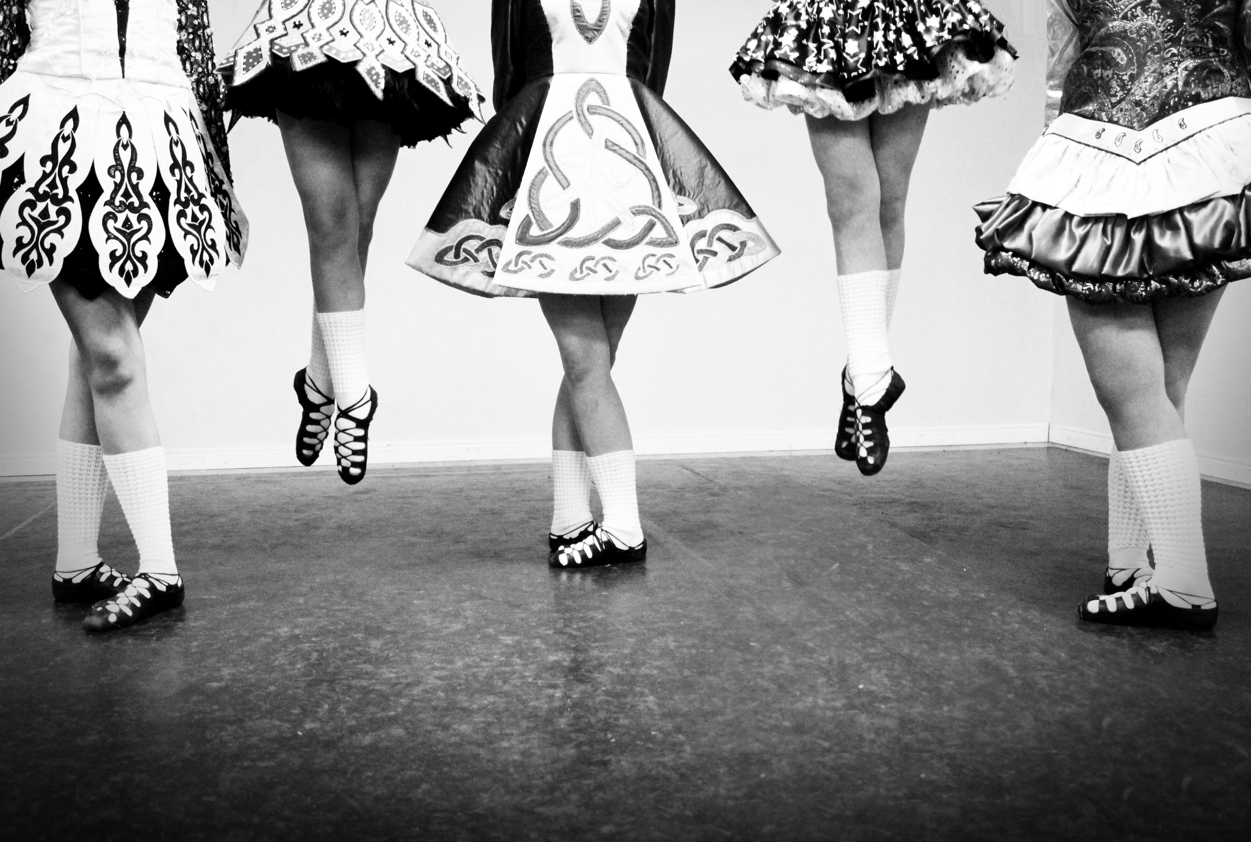 Black and white photo, 5 female Irish Dancers shown from the waist down, two in the air