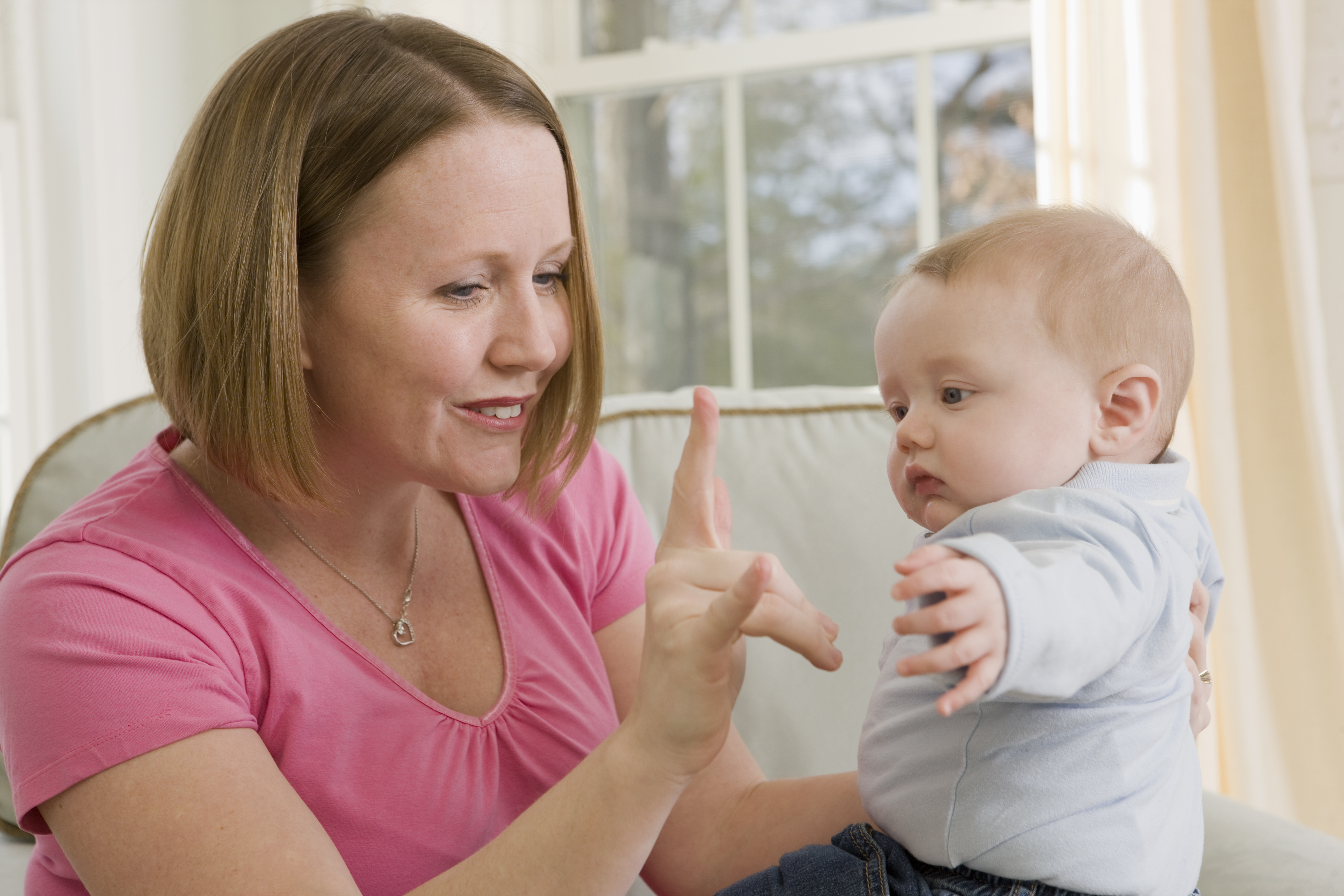 Woman signing the phrase "I love you" to baby in American Sign language