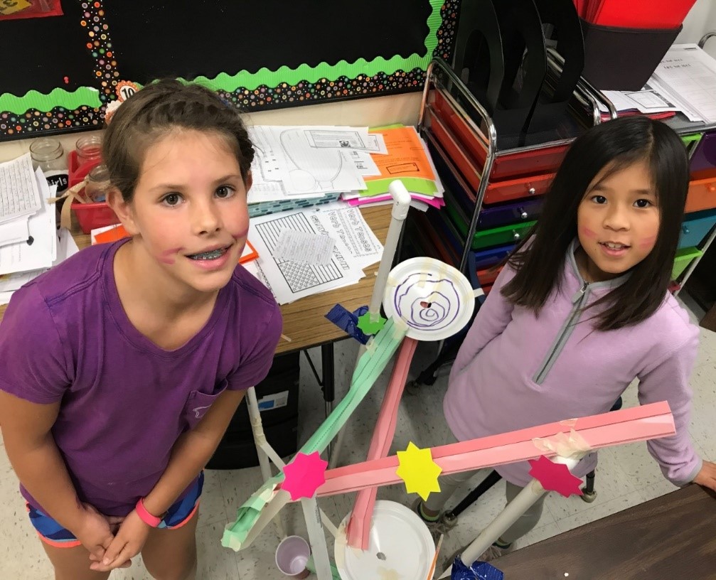 Two young girls are shown with the roller coaster model they built together