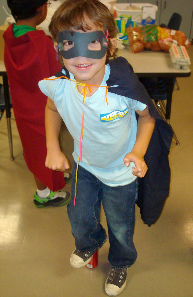 Young boy wearing a superhero cape and mask