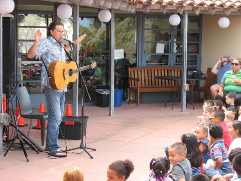 Man singing and playing a guitar in front of a library audience