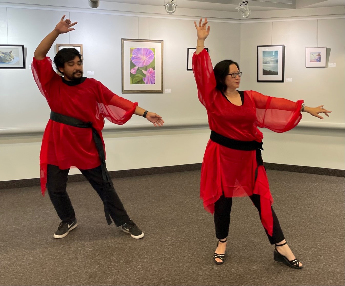 A man and woman in red dresses, dancing with their posed arms.