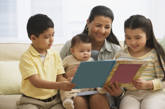 adult reading to two young children and a baby