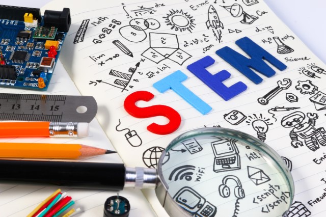 The letters STEM surrounded by doodles of science and technology images and materials