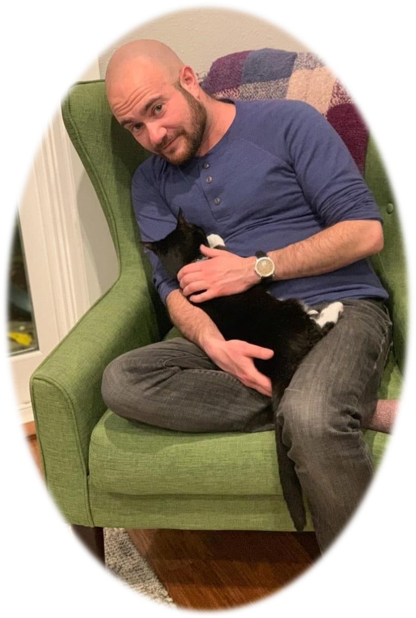 Image of Author Kyle Lukoff, author is wearing black jeans, a blue sweatshirt and is sitting on a neon green chair and holding a black cat in his lap.