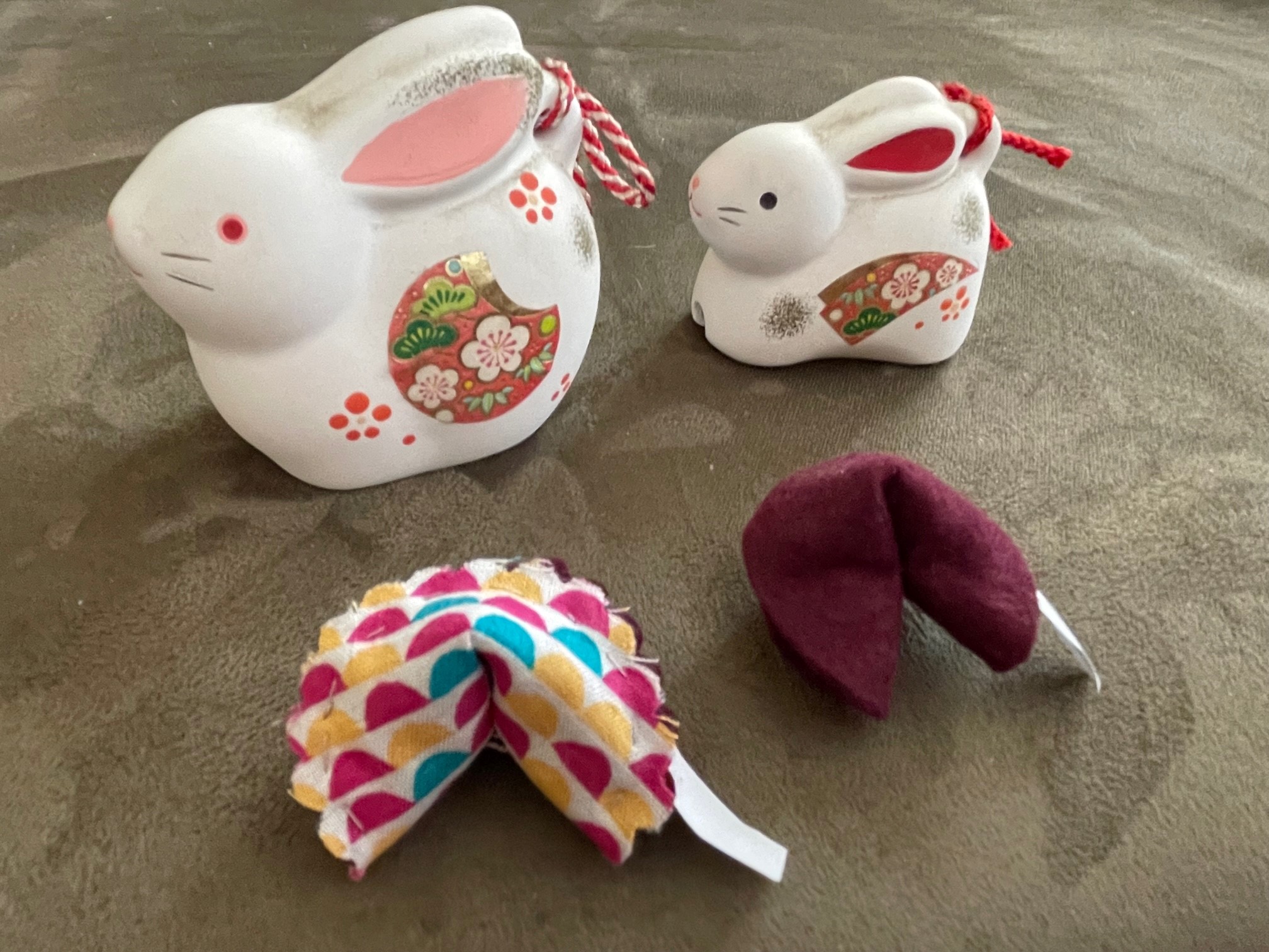 2 fortune cookies made out of fabric, in front of 2 ceramic rabbits