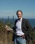 Photo of Dean Ratzman standing with a trumpet in front of the ocean