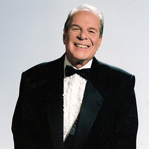 Photo of Richard Lederer in a black tuxedo on a light grey background