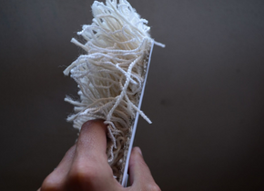 Photograph of a hand holding an artwork made of paper and white shag carpet by artist Antoni Szostak.