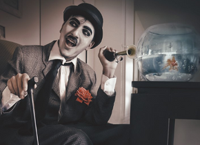 Photograph of a man in a suit with a bicycle horn sitting next to a goldfish in a bowl by artist Nathaly Alvizures. 