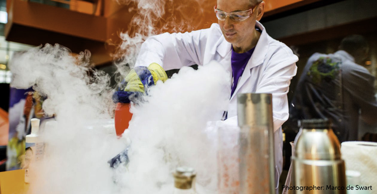 White coated gentleman with smoke billowing from beakers