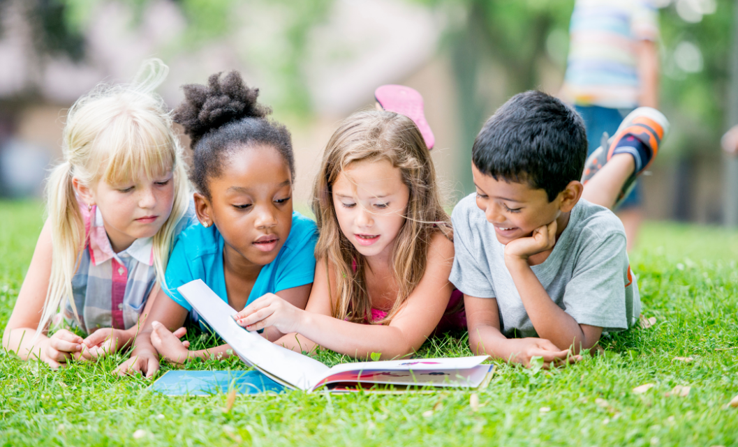children laying in grass reading a book