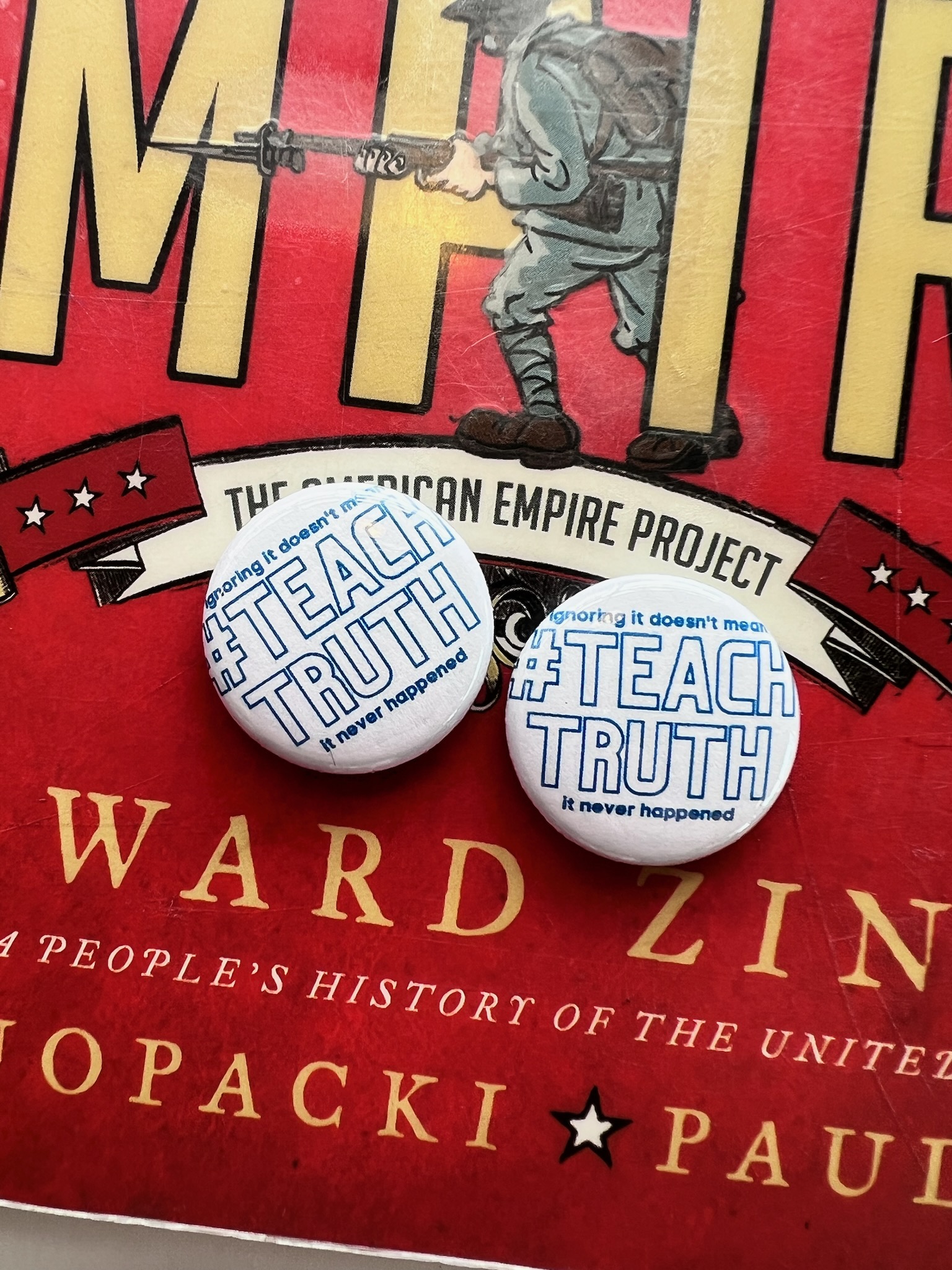 Two buttons that say "#TeachTruth" on top of a book by Howard Zinn