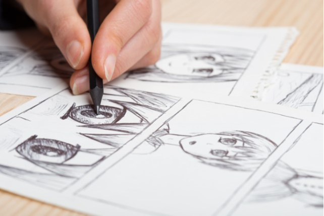 Image of someone holding pencil drawing manga characters.