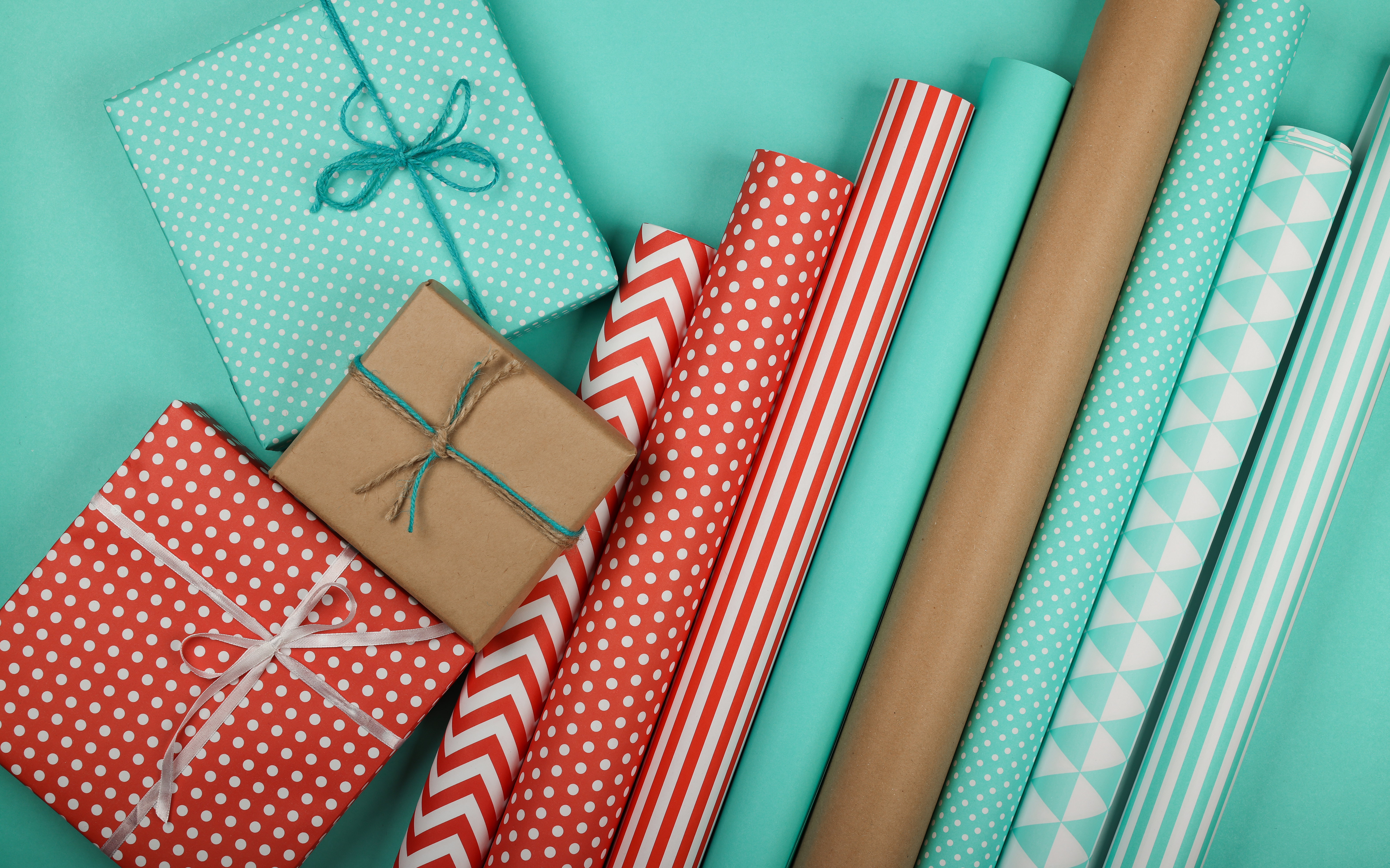 Gift wrap rolls and wrapped packages against a pale blue background