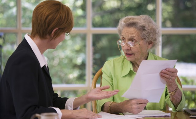 Senior female holding a paper and listening to another younger woman