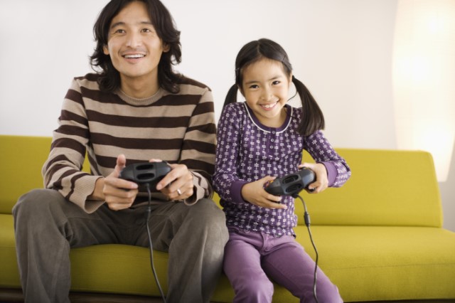 Father and daughter playing video games on a couch