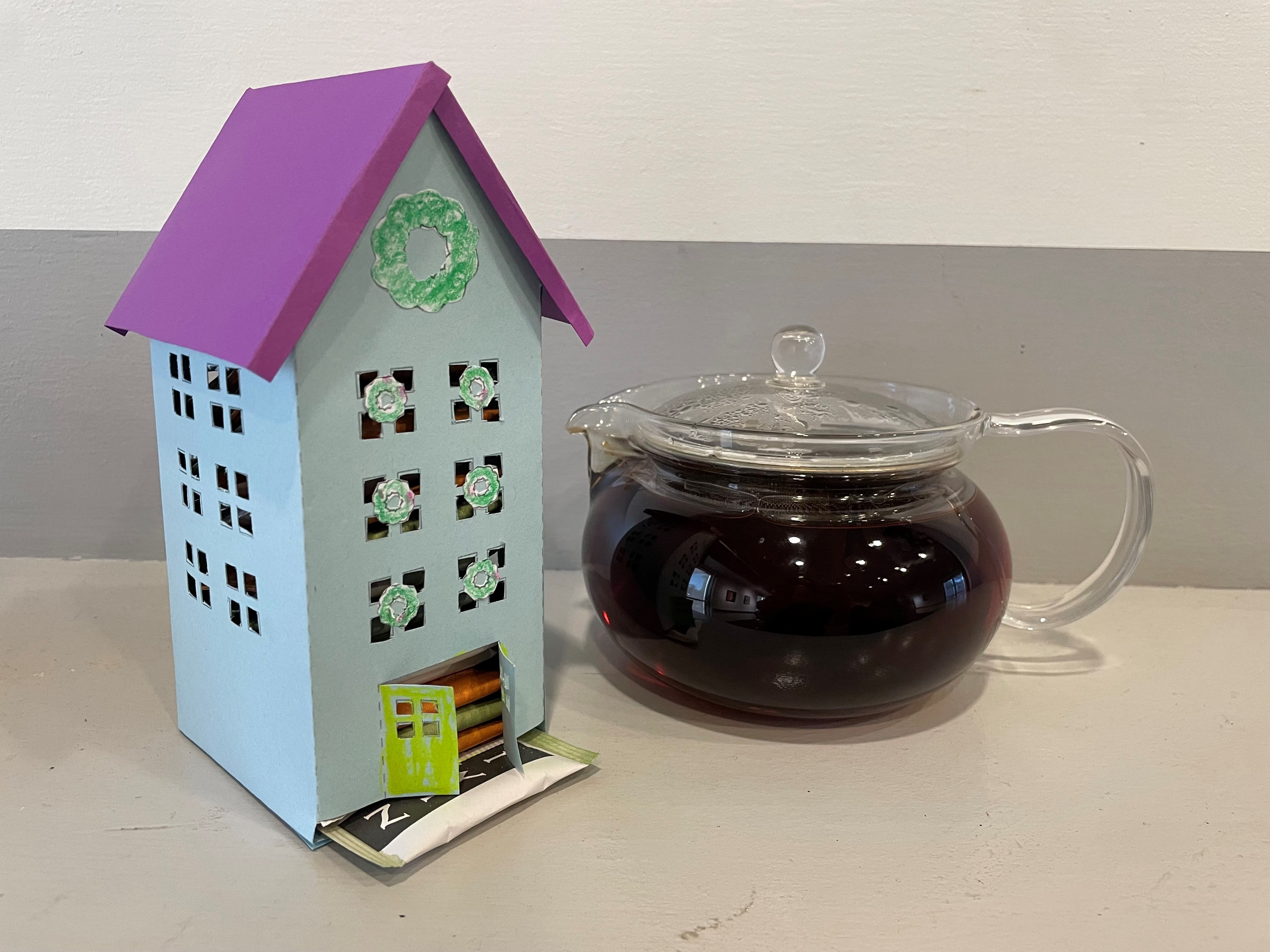 Tall paper house filled with tea bags, next to a tea pot