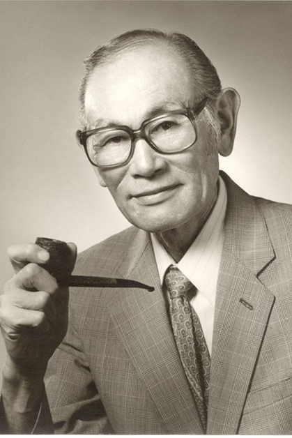 A black and white/sepia toned photo of Fred Korematsu holding a pipe.