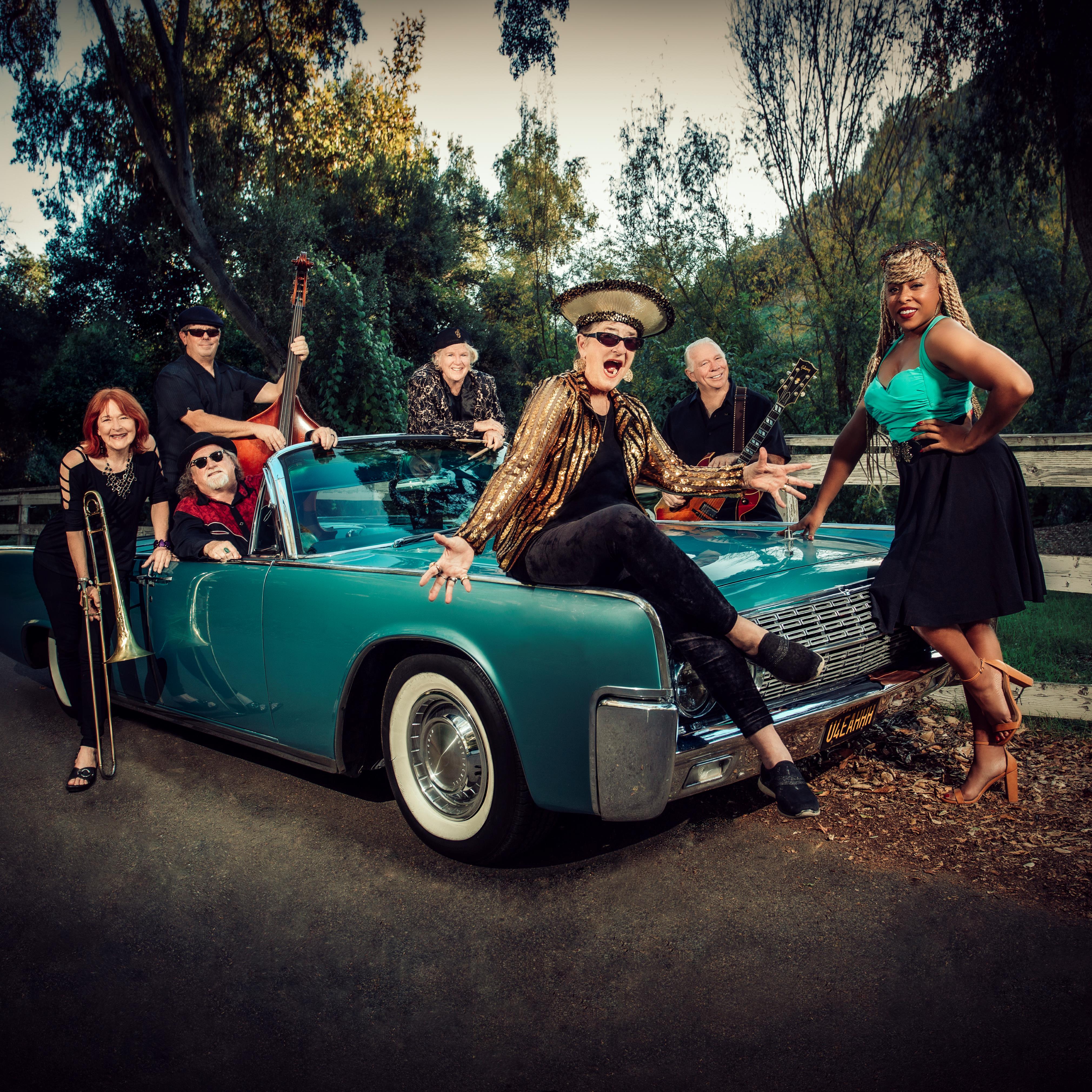 Sue Palmer and her ensemble seated and standing around a classic car