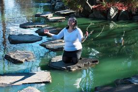 Woman kneeling on rock in lake.