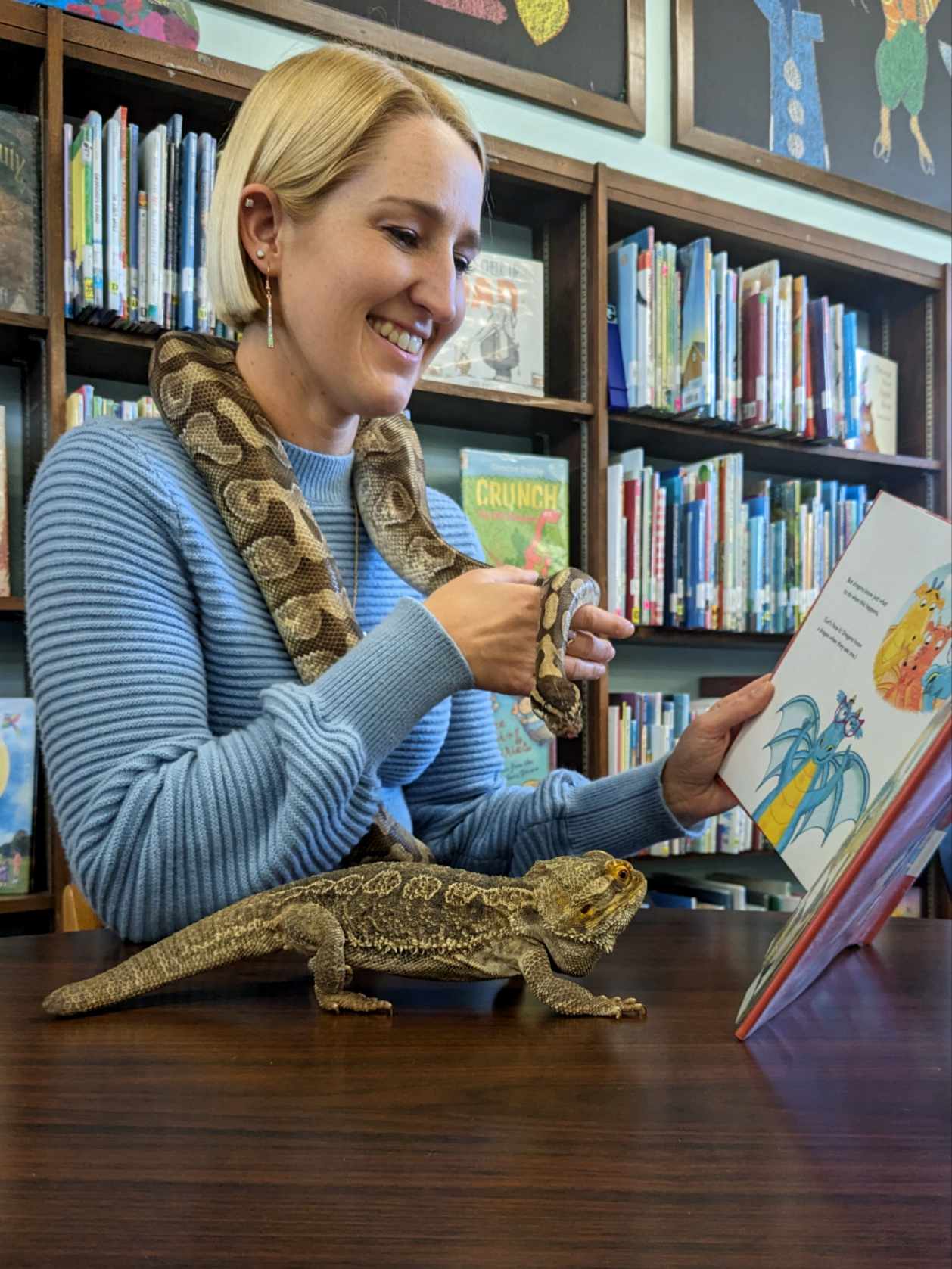 Ms. Camille reading to a bearded dragon and a ball python snake