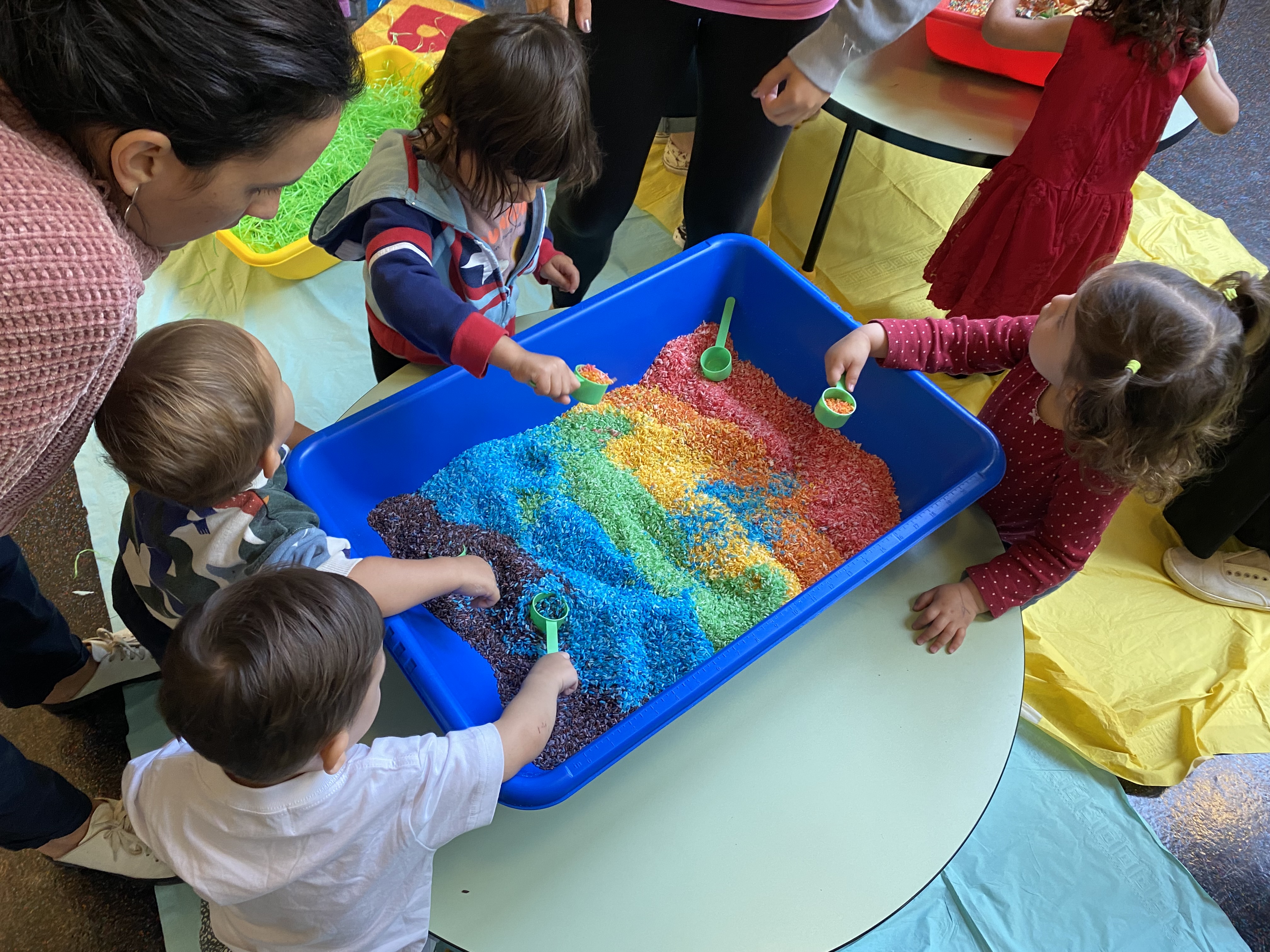 Preschoolers engaging in sensory play with rainbow rice and scoopers