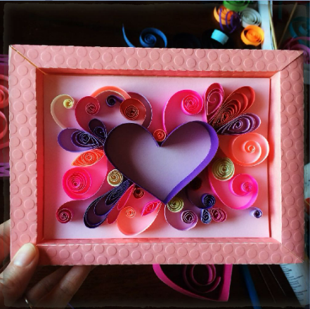 Photo of a paper quilling project in pinks and purples, in a pink frame