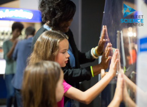 A woman and two children interacting with a science exhibit.