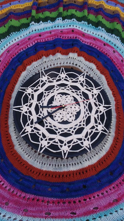 Image of a crocheted clock face, on top of a knitted circular piece with stripes.