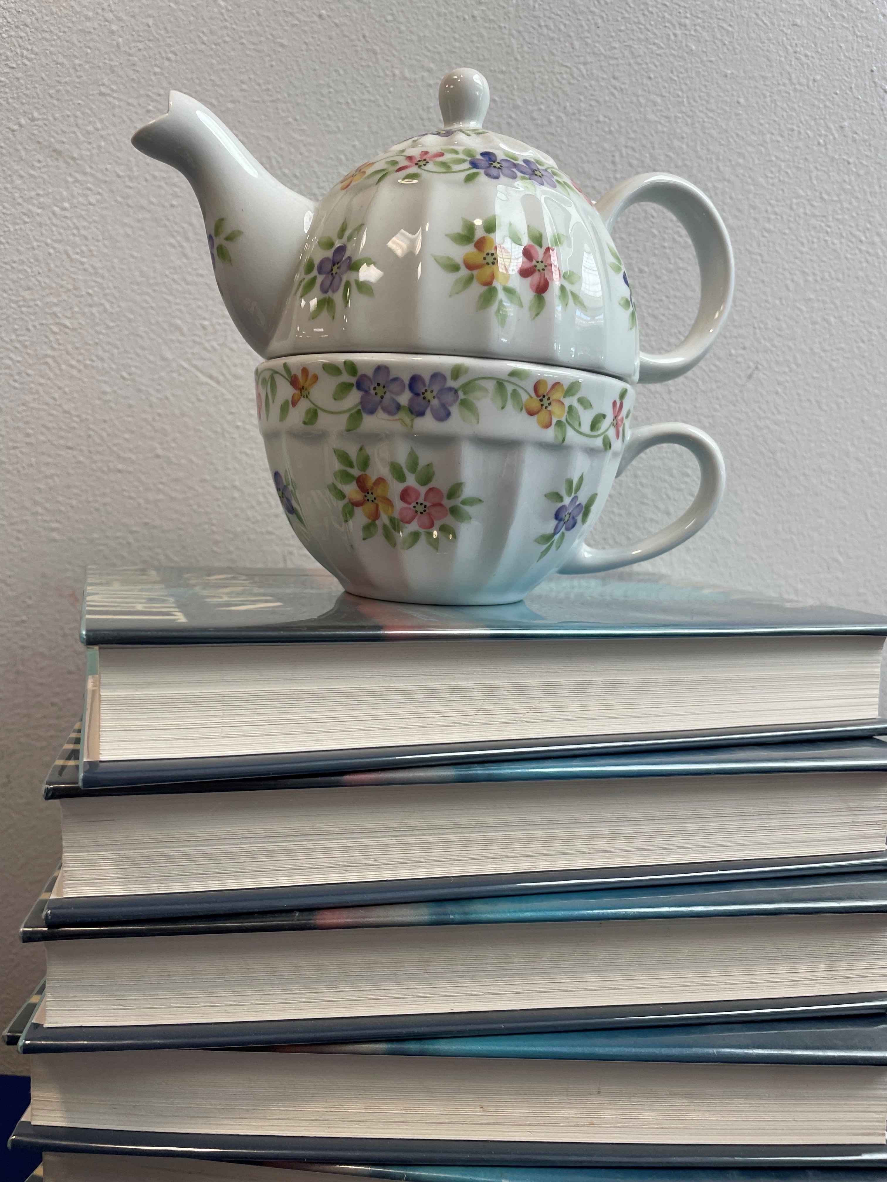 Teapot and teacup sitting on top of a stack of books.
