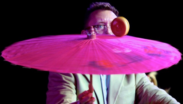 A man whose face is half-hidden by an umbrella, which he is spinning with a hamburger on top