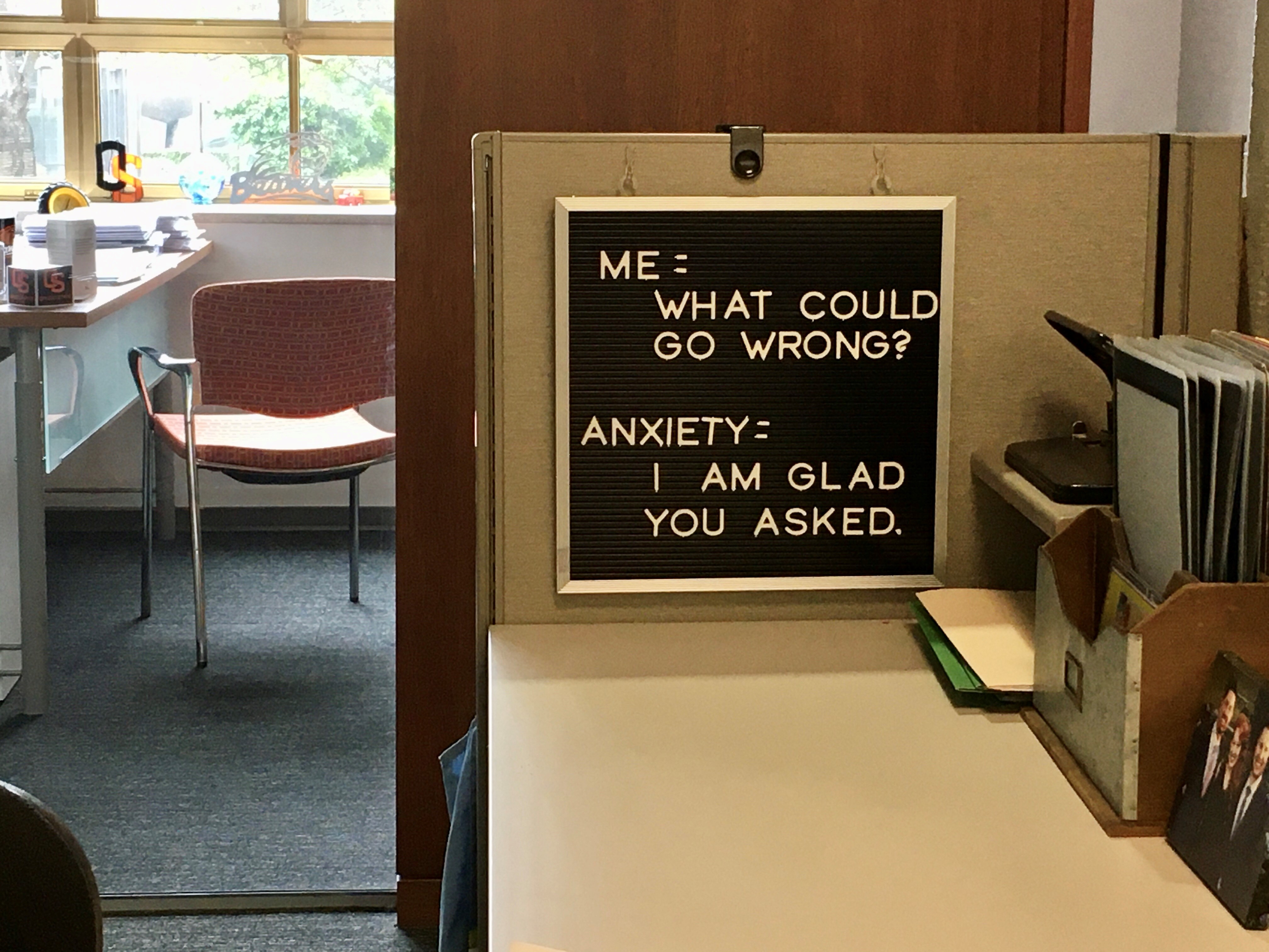 Photo of a letterboard in an office cubicle, reading "Me = What could go wrong? My anxiety = I'm glad you asked."